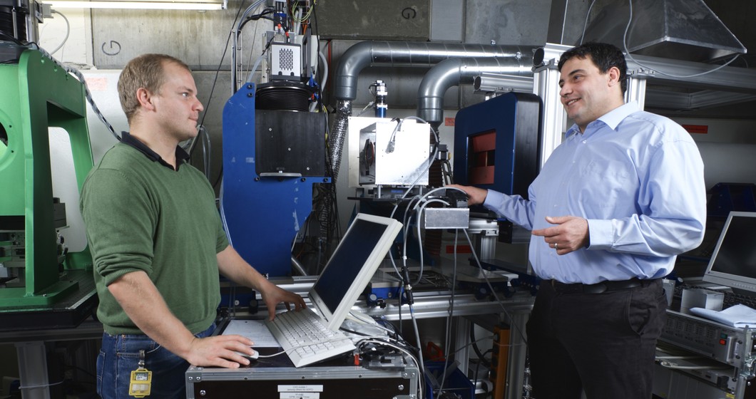 Benedikt Betz et Christian Grünzweig, chercheurs au PSI, à l’instrument aux neutrons qui leur permet d’étudier les processus magnétiques dans les noyaux de fer des transformateurs. (Photo: Institut Paul Scherrer/Markus Fischer)