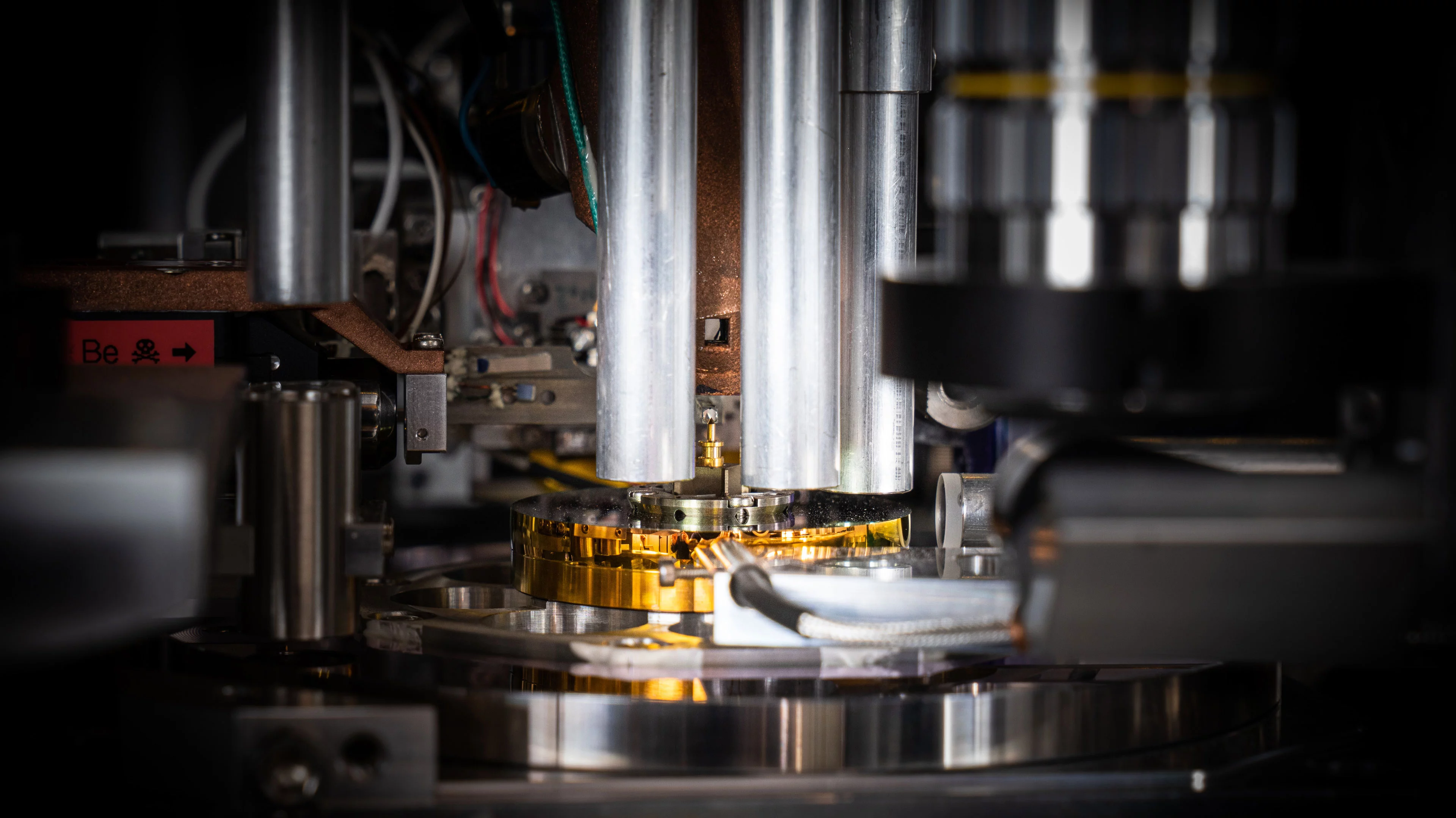 The sample, an extract from a commercial computer chip, is supported by the gold-coloured pin in the centre of the picture. Less than 0.000,005 metres in diameter (about 20 times smaller than the width of a human hair), it was cut out of the chip using a focused ion beam and placed on the pin.