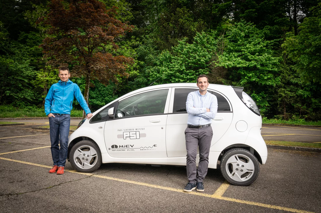 Christian Bauer and Romain Sacchi stand in front of an electric car which has the PSI logo.