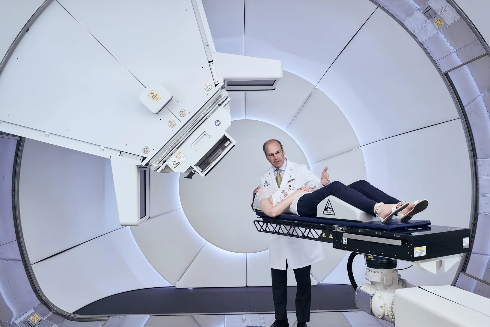 Gantry 3 – the new treatment unit for proton therapy at PSI. A staff member of PSI demonstrates the patient positioning. Standing: Prof. Damien Weber, head of the Centre for Proton Therapy at the Paul Scherrer Institute. (Photo: Scanderbeg Sauer Photography)